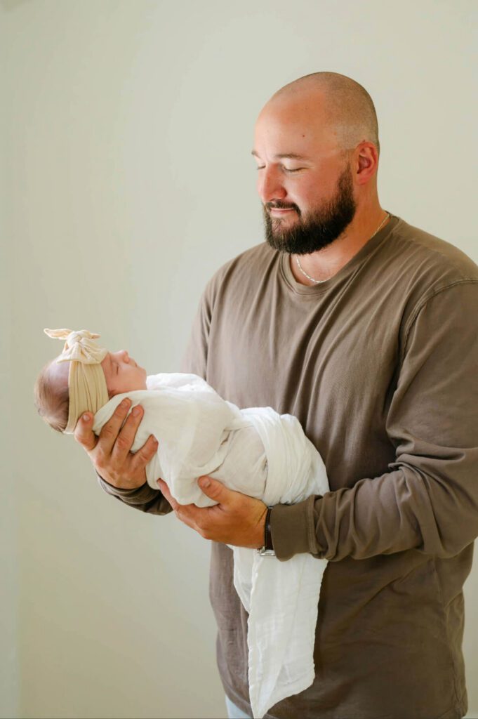 Dad holds swaddled newborn baby girl looking down at her