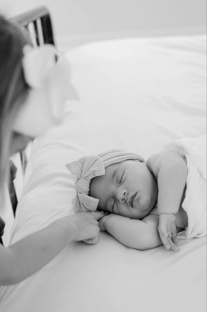 Toddler sister holding newborn baby's hand in black and white photo